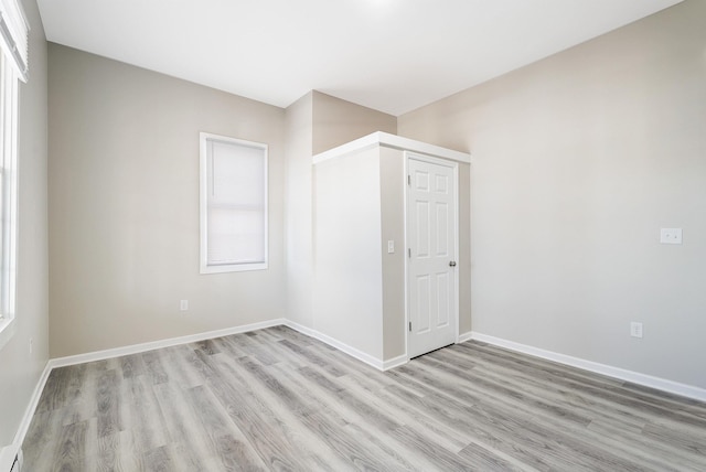 unfurnished room with a baseboard heating unit, a wealth of natural light, and light wood-type flooring