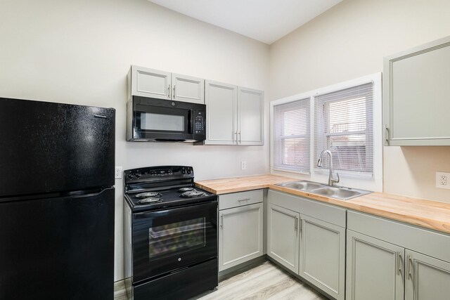 kitchen with sink, wooden counters, light wood-type flooring, and black appliances