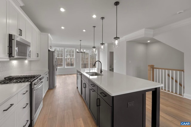 kitchen with a sink, light wood-style floors, a kitchen island with sink, white cabinetry, and appliances with stainless steel finishes