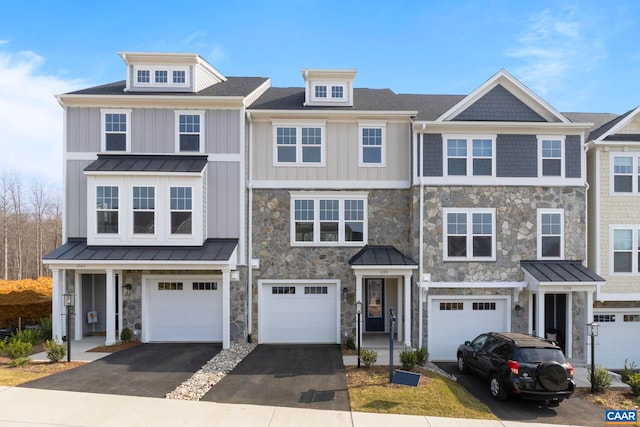 townhome / multi-family property featuring stone siding, an attached garage, board and batten siding, driveway, and a standing seam roof