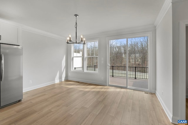 unfurnished dining area with an inviting chandelier, ornamental molding, a wealth of natural light, and light wood-style flooring