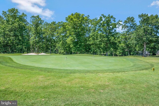 view of property's community with view of golf course, view of wooded area, an area to practice putting, and a lawn