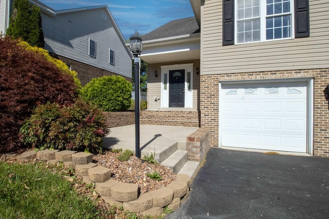 property entrance with brick siding, an attached garage, and driveway
