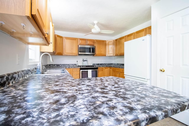 kitchen with stainless steel appliances, dark countertops, a sink, ceiling fan, and a peninsula