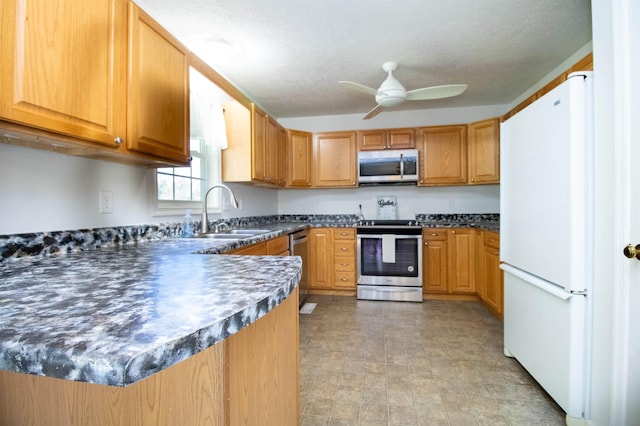 kitchen with appliances with stainless steel finishes, a sink, ceiling fan, dark countertops, and a peninsula