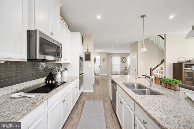 kitchen featuring stainless steel appliances, light wood-style floors, a sink, white cabinetry, and tasteful backsplash