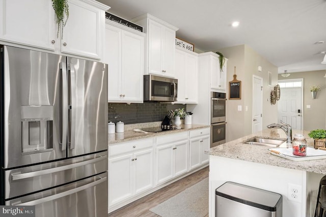 kitchen featuring appliances with stainless steel finishes, a sink, white cabinetry, light wood-style floors, and tasteful backsplash