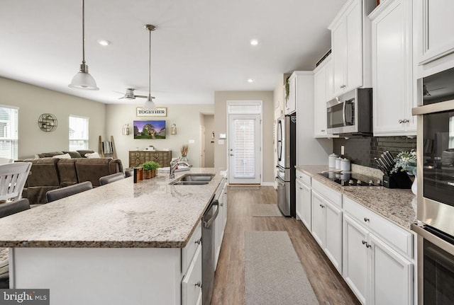 kitchen featuring stainless steel appliances, a sink, dark wood-type flooring, white cabinets, and a kitchen island with sink