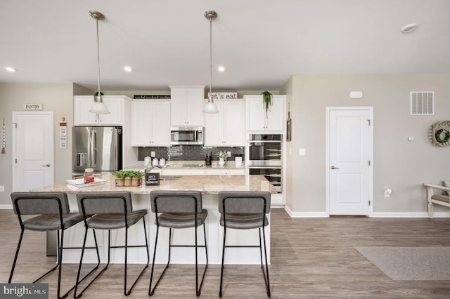 kitchen featuring appliances with stainless steel finishes, a kitchen island with sink, baseboards, white cabinets, and recessed lighting