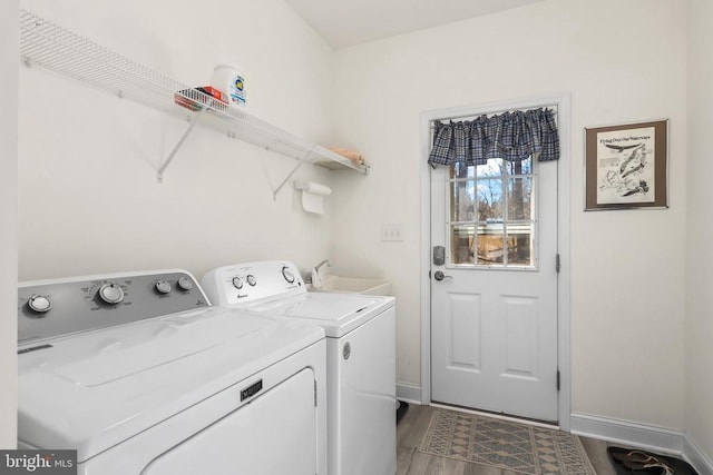 clothes washing area featuring washing machine and dryer, wood finished floors, and baseboards