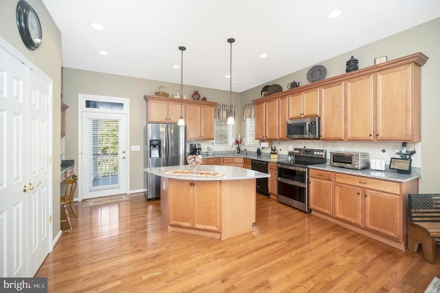 kitchen with appliances with stainless steel finishes, a center island, light wood-style flooring, pendant lighting, and light stone countertops