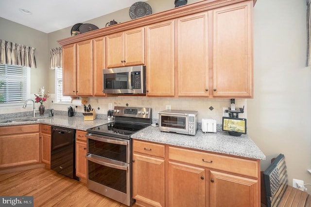 kitchen with stainless steel appliances, a sink, light wood finished floors, and light stone countertops