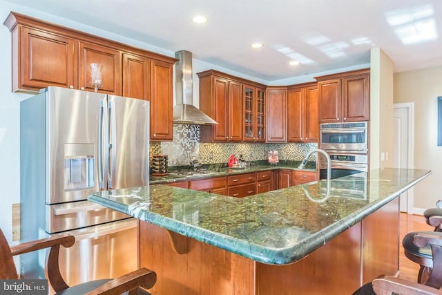 32314 Deep Meadow Ln, Locust Grove, VA 22508 - kitchen with appliances with stainless steel finishes, wall chimney range hood, decorative backsplash, a kitchen breakfast bar, and brown cabinets