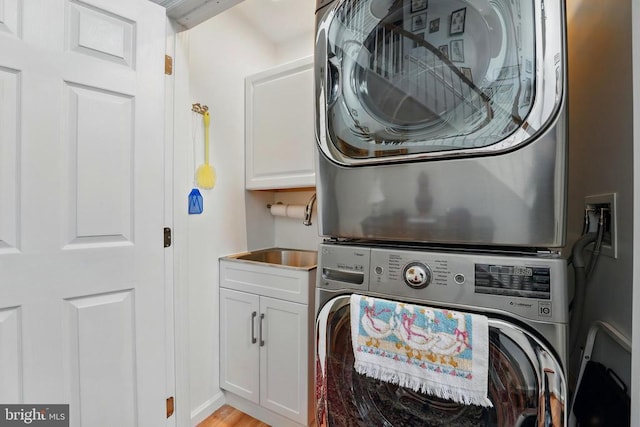 clothes washing area with stacked washer / dryer, cabinet space, and light wood-style floors