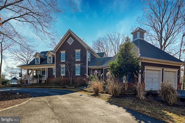 traditional-style house with covered porch, aphalt driveway, roof with shingles, and a garage