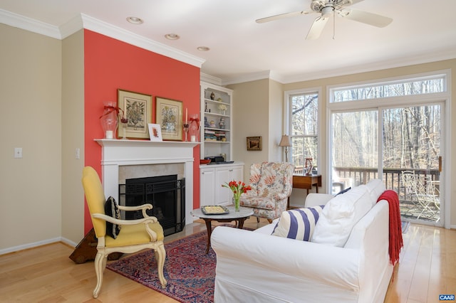 living room featuring a fireplace, light wood finished floors, ornamental molding, a ceiling fan, and baseboards