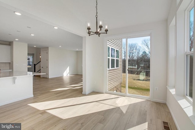 unfurnished dining area featuring light wood finished floors, a chandelier, recessed lighting, stairway, and baseboards