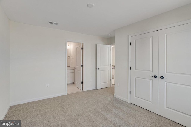 unfurnished bedroom featuring light carpet, a closet, baseboards, and ensuite bathroom