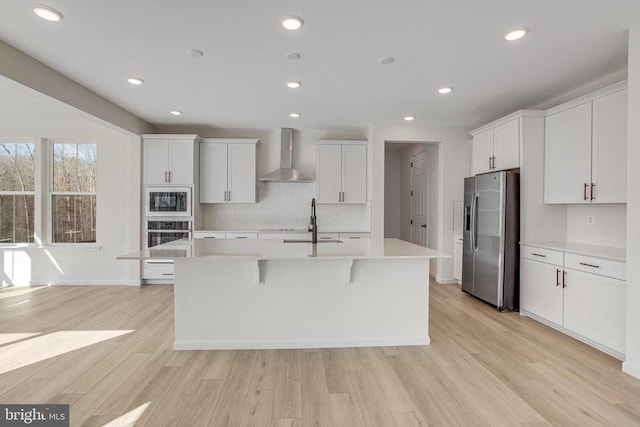 kitchen with stainless steel appliances, wall chimney range hood, light countertops, a center island with sink, and a sink