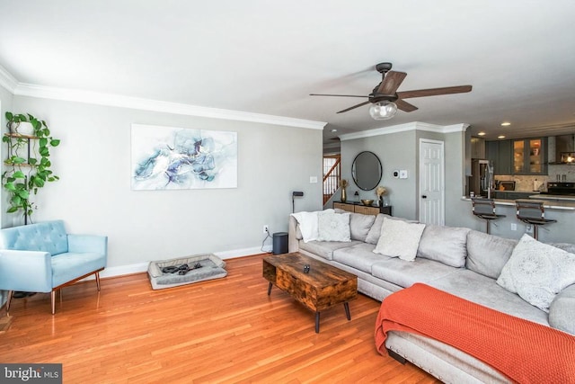 living area with a ceiling fan, light wood-style floors, ornamental molding, and baseboards