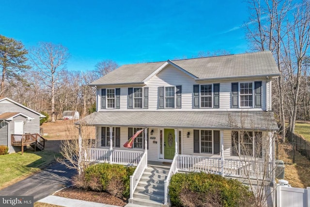 view of front of house featuring covered porch, fence, a shingled roof, and stairway