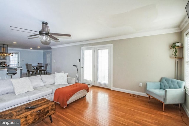 living area featuring crown molding, light wood-type flooring, baseboards, and ceiling fan with notable chandelier