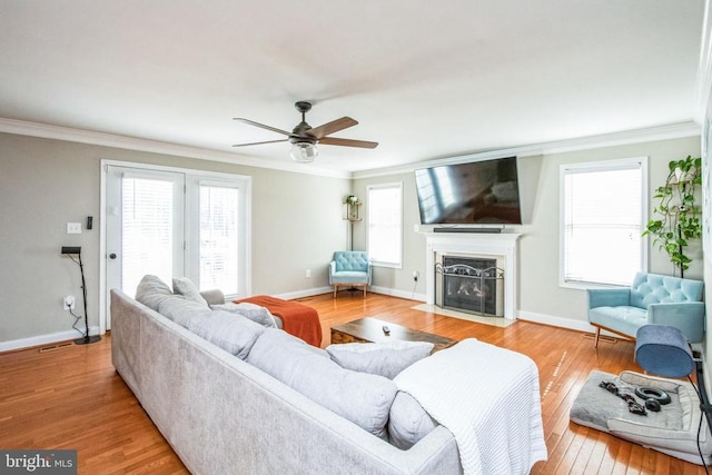 living room featuring wood finished floors, ornamental molding, a ceiling fan, baseboards, and a fireplace with flush hearth