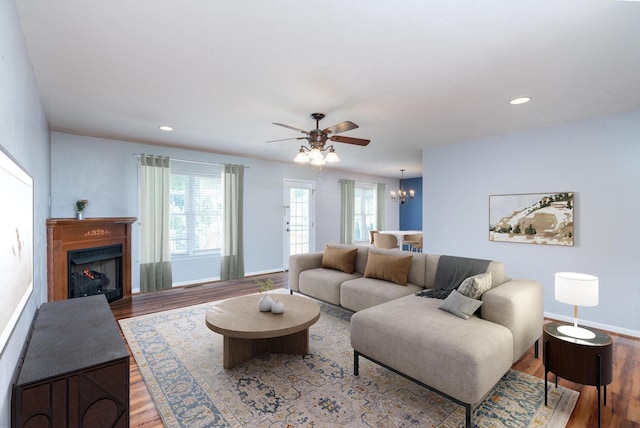 living room featuring wood finished floors, a chandelier, ceiling fan, baseboards, and a fireplace