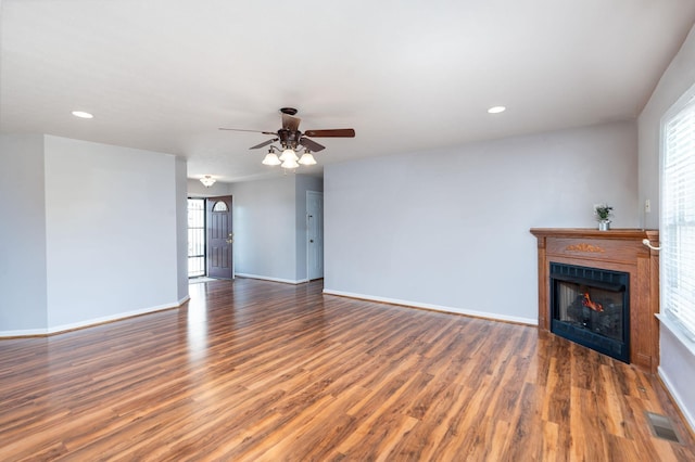 unfurnished living room with wood finished floors, a warm lit fireplace, ceiling fan, baseboards, and recessed lighting
