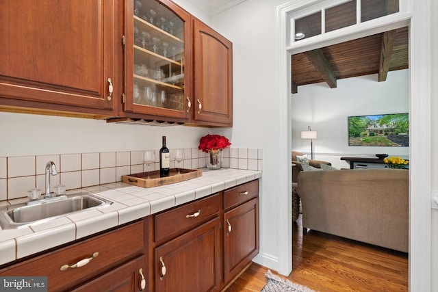  - kitchen with a sink, light wood finished floors, glass insert cabinets, brown cabinetry, and backsplash