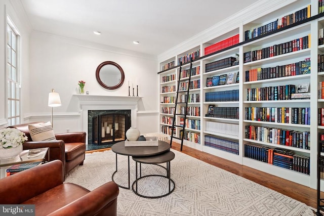 - sitting room featuring wood finished floors, a high end fireplace, ornamental molding, built in shelves, and bookshelves