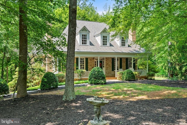  - new england style home with covered porch, brick siding, and a chimney