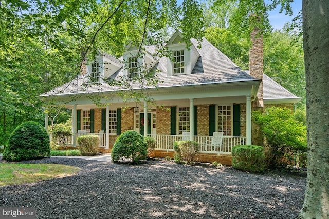  - cape cod house featuring a porch, brick siding, and a chimney