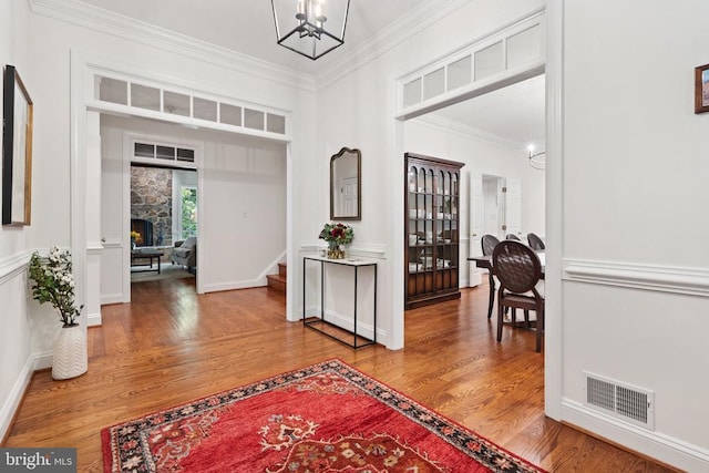  - entrance foyer with a chandelier, wood finished floors, ornamental molding, stairs, and a stone fireplace