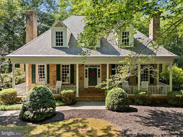 - view of front facade featuring a chimney, covered porch, and brick siding