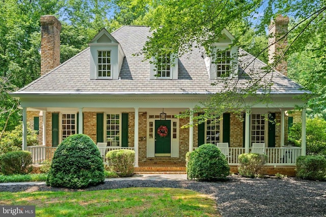 - view of front of house featuring a chimney, covered porch, brick siding, and a high end roof