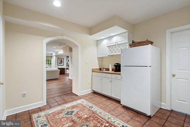  - kitchen featuring freestanding refrigerator, arched walkways, light tile patterned floors, white cabinets, and recessed lighting