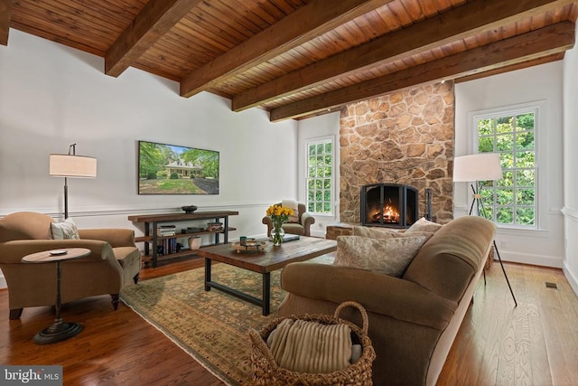  - living room with wooden ceiling with exposed beams, healthy amount of natural light, wood finished floors, and a stone fireplace