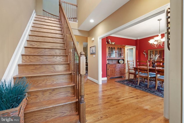  - stairs with a chandelier, wood finished floors, and ornamental molding