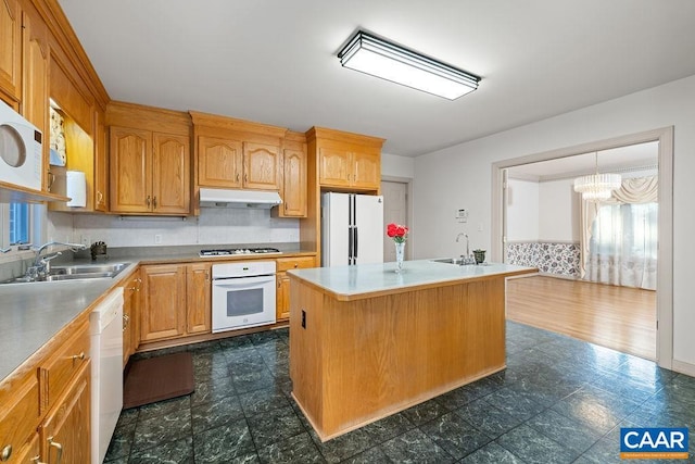 kitchen featuring under cabinet range hood, an island with sink, a sink, and white appliances