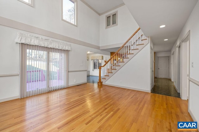 unfurnished living room featuring a towering ceiling, wood finished floors, baseboards, and stairs