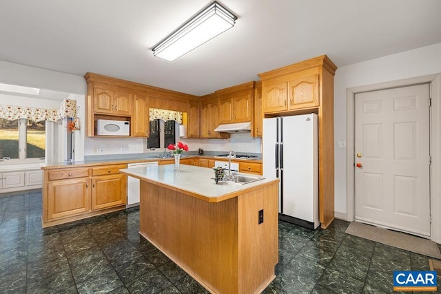 kitchen with a sink, white appliances, under cabinet range hood, light countertops, and a kitchen island
