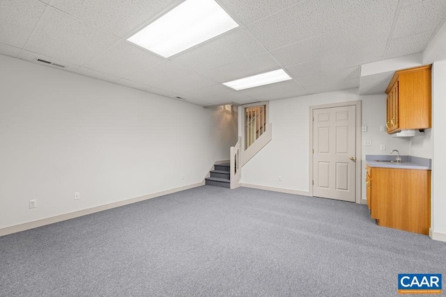 finished below grade area featuring stairs, light carpet, baseboards, and a paneled ceiling