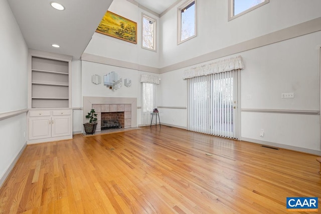 unfurnished living room with a tiled fireplace, light wood-style flooring, baseboards, and a high ceiling