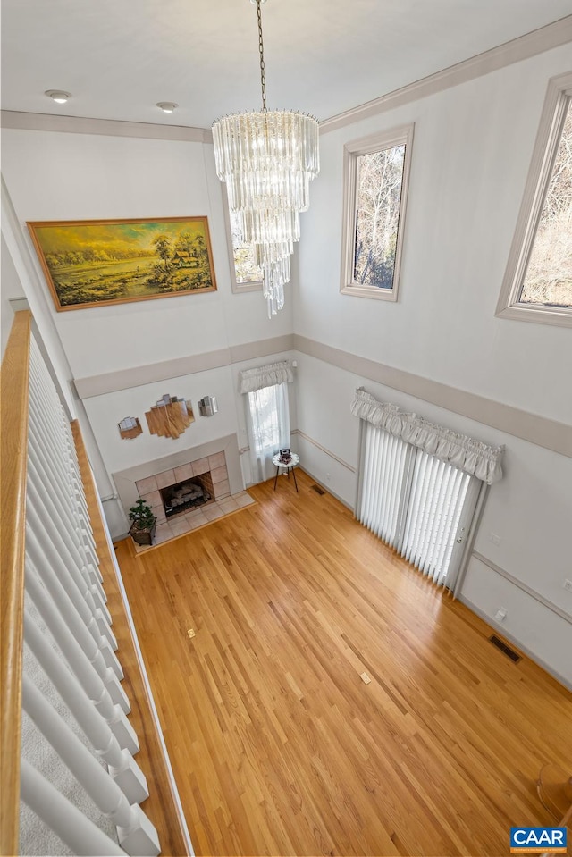 unfurnished living room featuring wood finished floors, a notable chandelier, visible vents, ornamental molding, and radiator heating unit