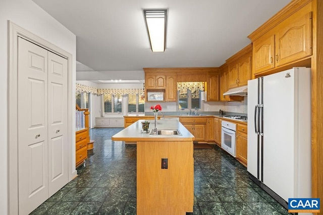 kitchen with a sink, white appliances, under cabinet range hood, and light countertops
