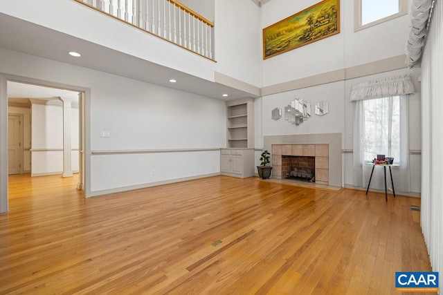 unfurnished living room featuring baseboards, hardwood / wood-style floors, a tiled fireplace, and a towering ceiling