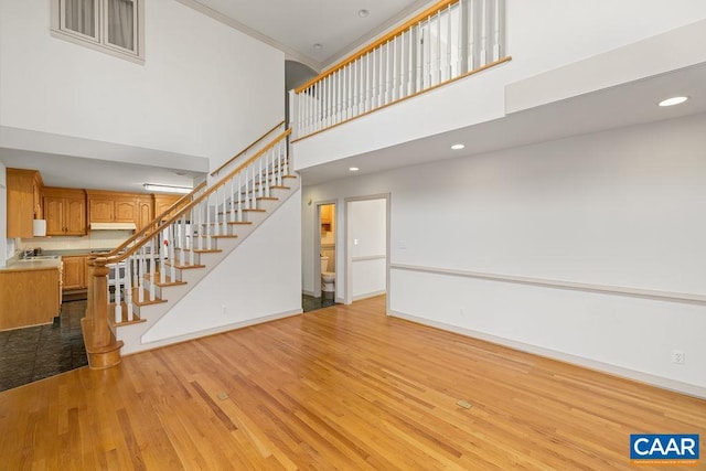 unfurnished living room featuring recessed lighting, baseboards, stairs, wood finished floors, and a high ceiling