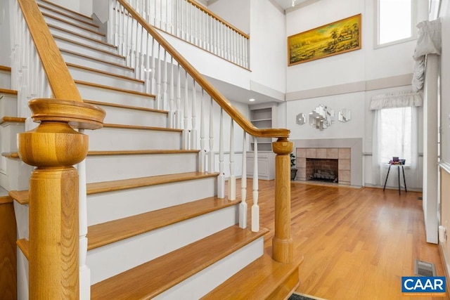 stairway with a tiled fireplace, a high ceiling, visible vents, and wood finished floors