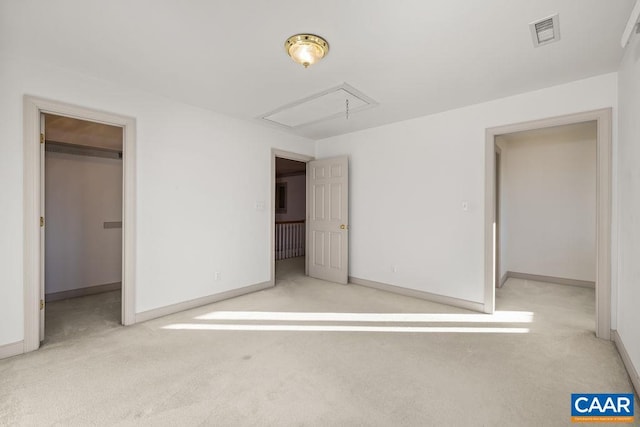 unfurnished bedroom with a walk in closet, attic access, carpet floors, and visible vents